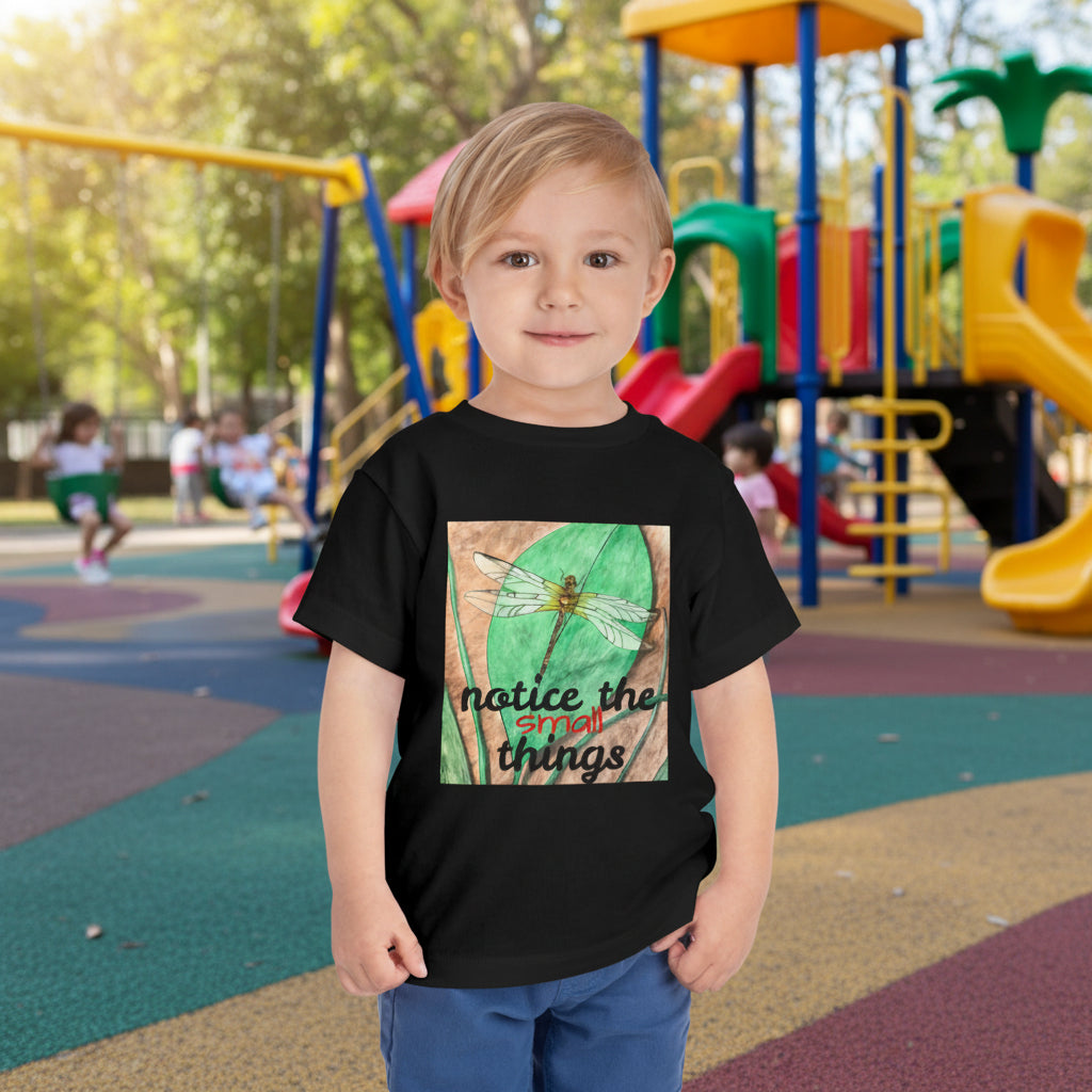 Child wearing a black t-shirt with a dragonfly on a leaf graphic and text at a playground