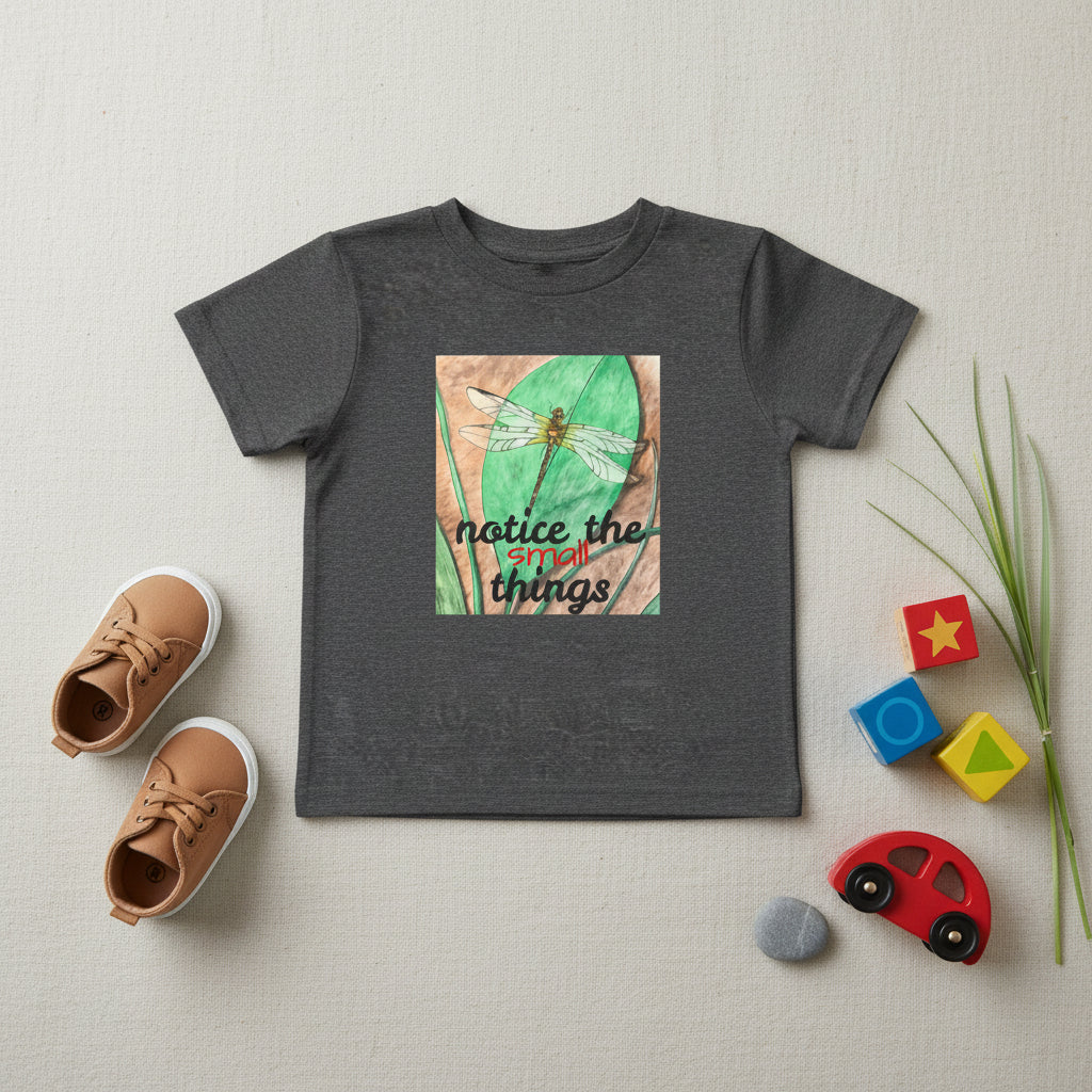A dark heather gray short-sleeve t-shirt with a square graphic print on the front. The graphic features a watercolor dragonfly on a green leaf with the text 'notice the small things' in black and red script.