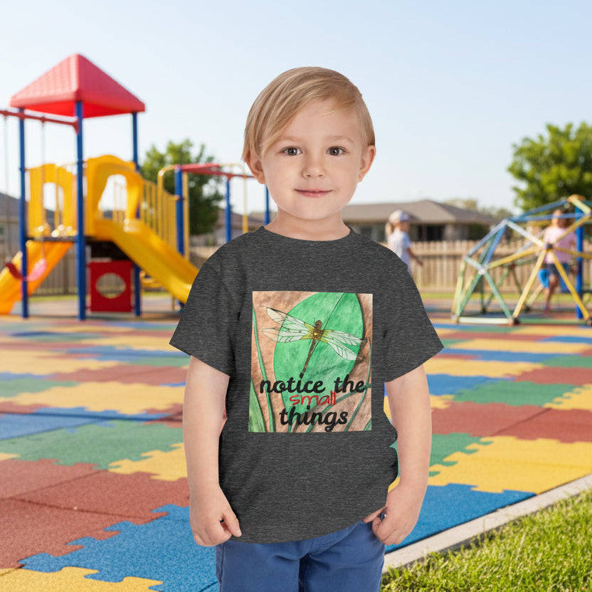 Child wearing a dark gray t-shirt with a dragonfly graphic and text on school playground