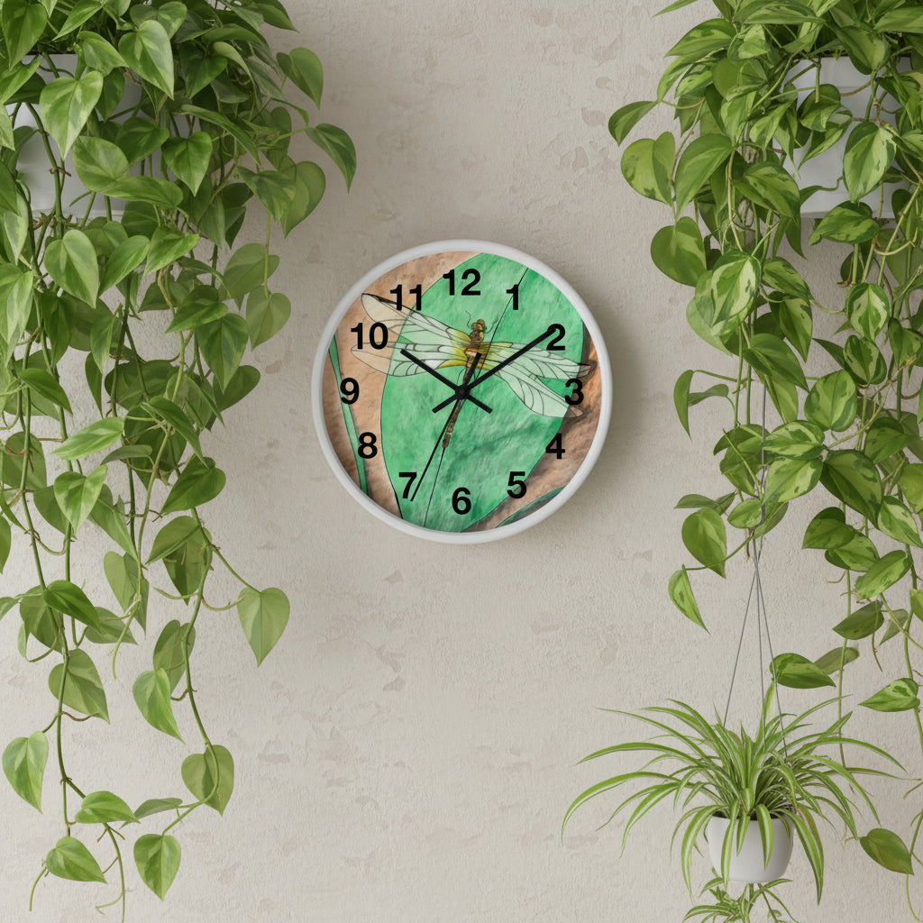 Wall clock with a dragonfly design on a green and brown background on on wall with hanging plants on the sides.