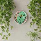 Wall clock with a dragonfly design on a green and brown background on on wall with hanging plants on the sides.