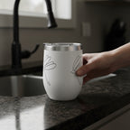 White tumbler with Dragonfly Stick Drawing shown on the side with a hand grabbing it by a kitchen sink