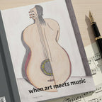 Open notebook with a guitar and half woman's back illustration and text 'when art meets music' laid flat on a desk with a fountain pen and a music sheet