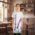 A woman modeling a white apron with a purple lavender and green leaf botanical print over a faint cursive script background, set in a cafe