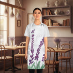 A woman modeling a white apron with a purple lavender and green leaf botanical print over a faint cursive script background, set in a cafe