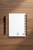 back of notebook with black spiral binding on a medium brown desk with a pen next to it