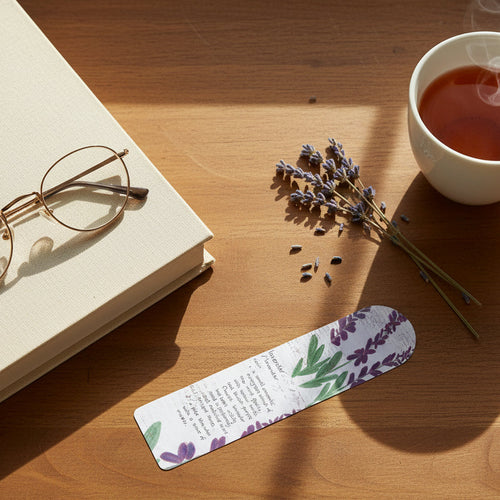 Decorative bookmark with lavender design and text on desk with hot drink, a book with reading glasses