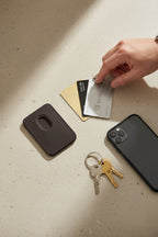 Black rectangular cardholder with rounded corners with a man's hand on a few credit cards with keys and phone next to it.