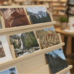 A wooden display rack holding multiple landscape and nature photographs in a softly blurred bookstore or gallery setting.