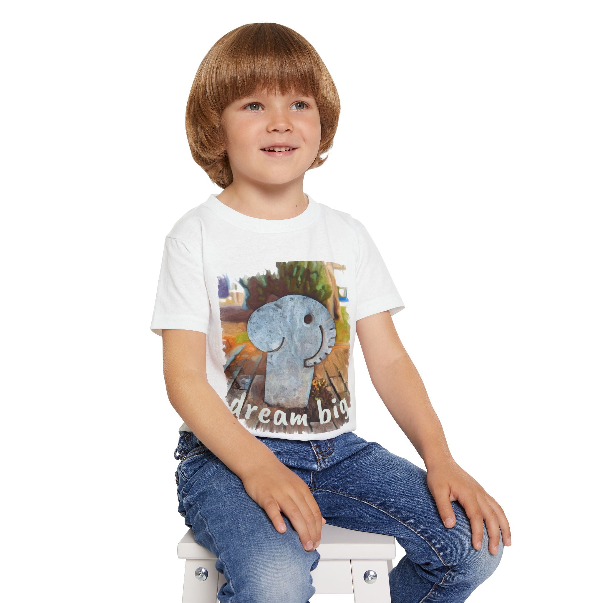 Child wearing a white t-shirt with an elephant graphic and 'Dream Big' text, sitting on a white stool.