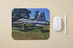 Painting of a vintage Air Force airplane on grass with trees in the background on a light wood desk with a mouse and stylus next to it.