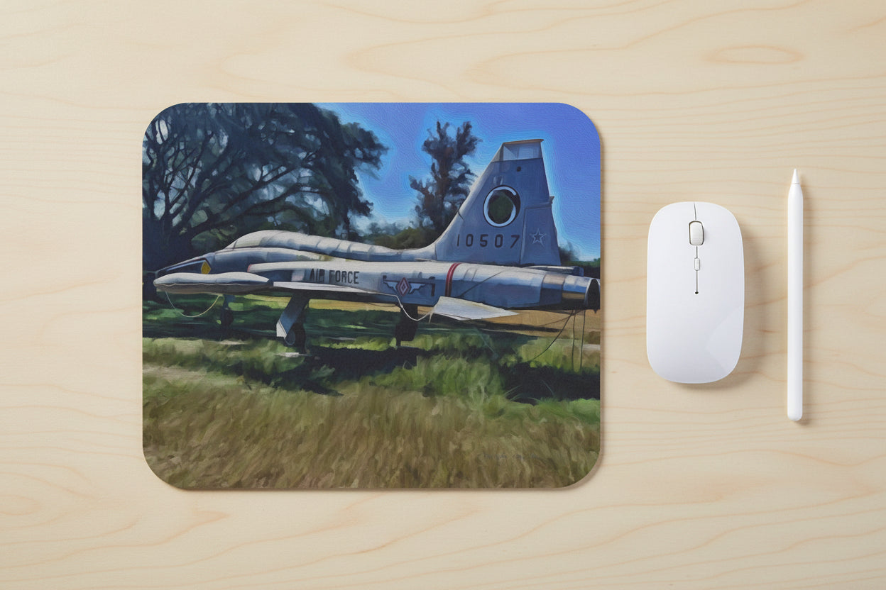 Painting of a vintage Air Force airplane on grass with trees in the background on a light wood desk with a mouse and stylus next to it.