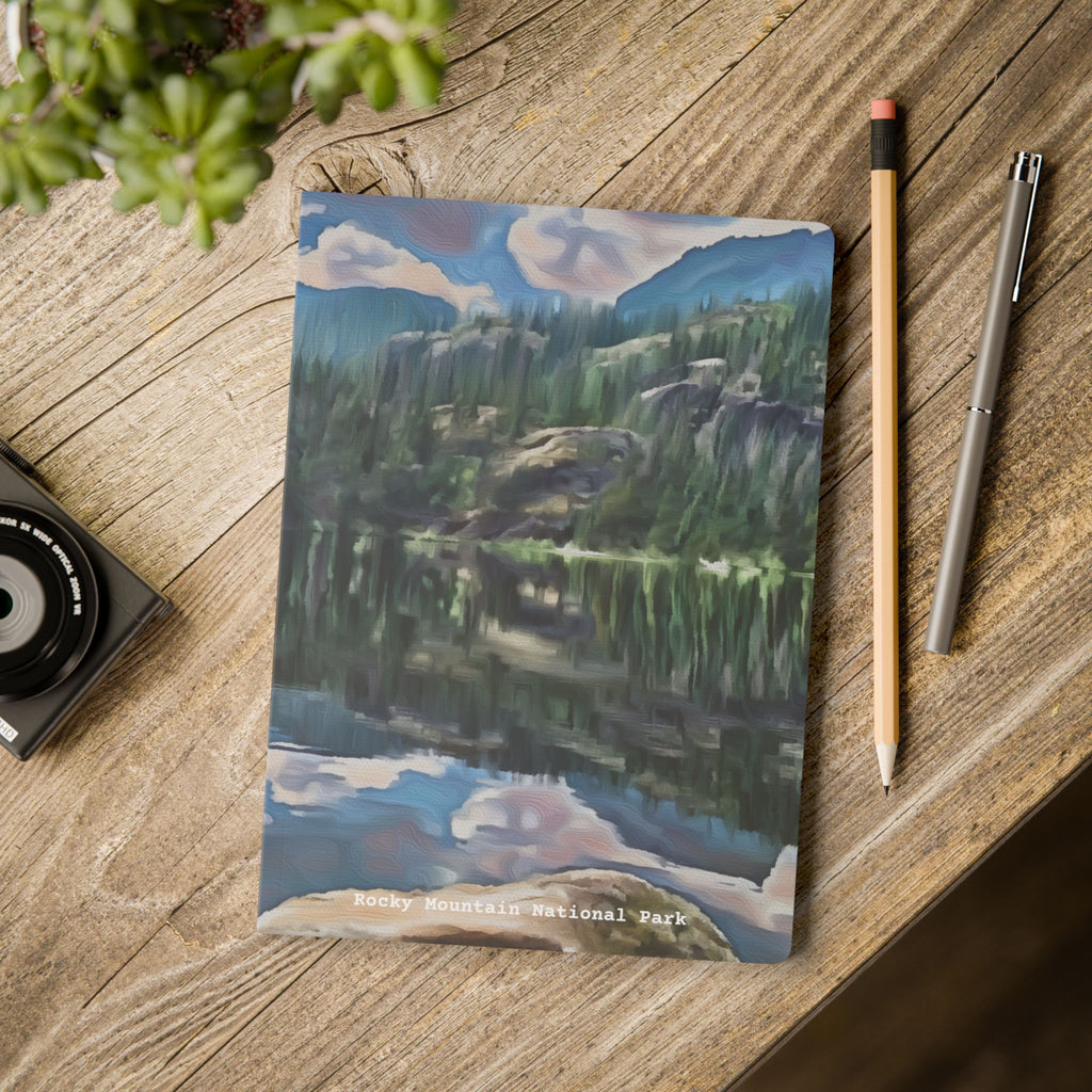 Notebook with a mountain landscape design on a wooden surface with a pen and pencil.