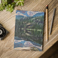 Notebook with a mountain landscape design on a wooden surface with a pen and pencil.