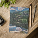 Notebook with a mountain landscape design on a wooden surface with a pen and pencil.