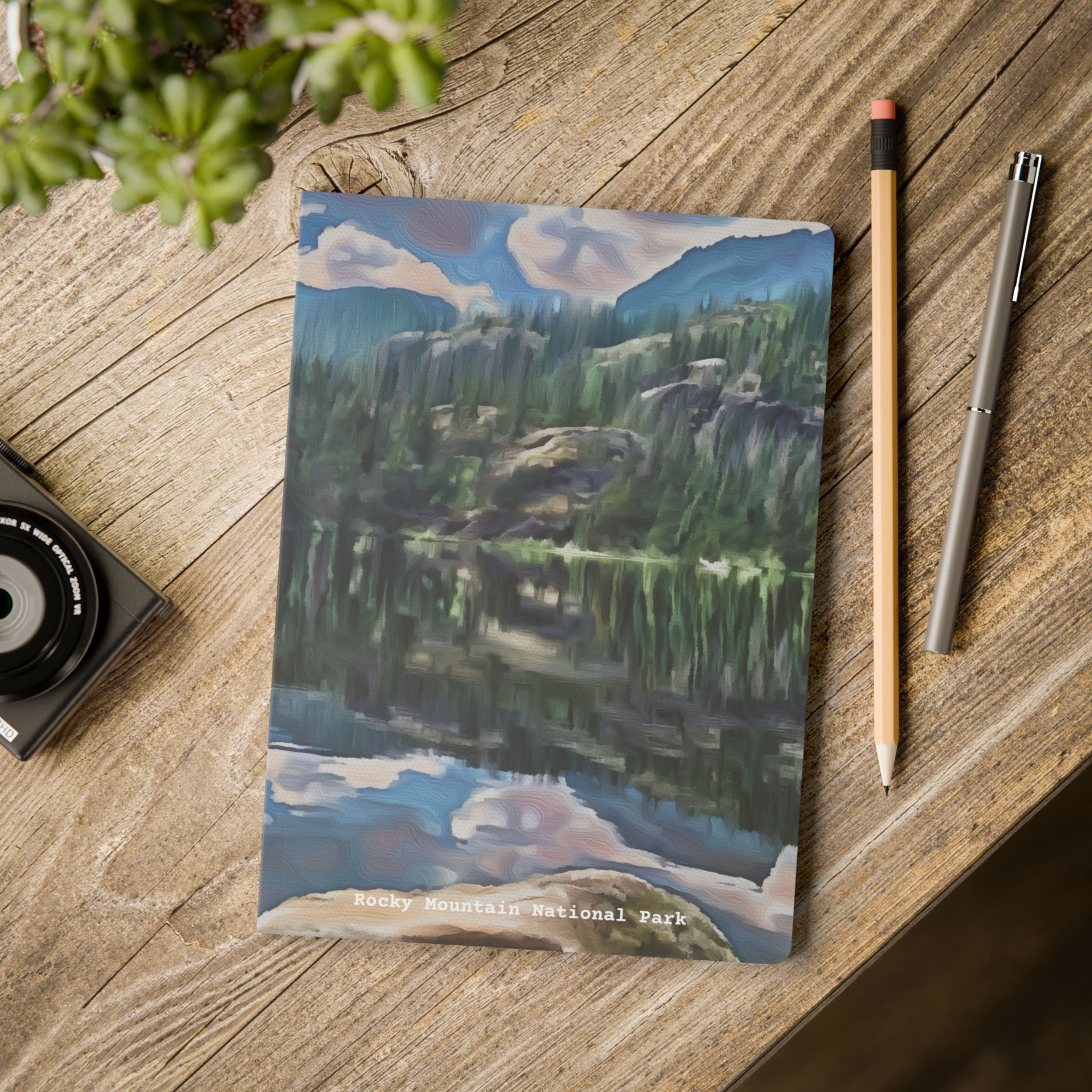 Notebook with a mountain landscape design on a wooden surface with a pen and pencil.