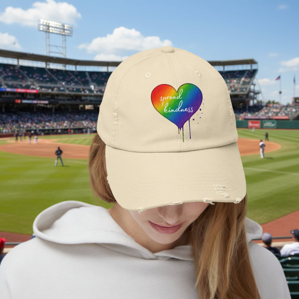 Beige cap with rainbow heart design and 'spread kindness' text at a baseball game
