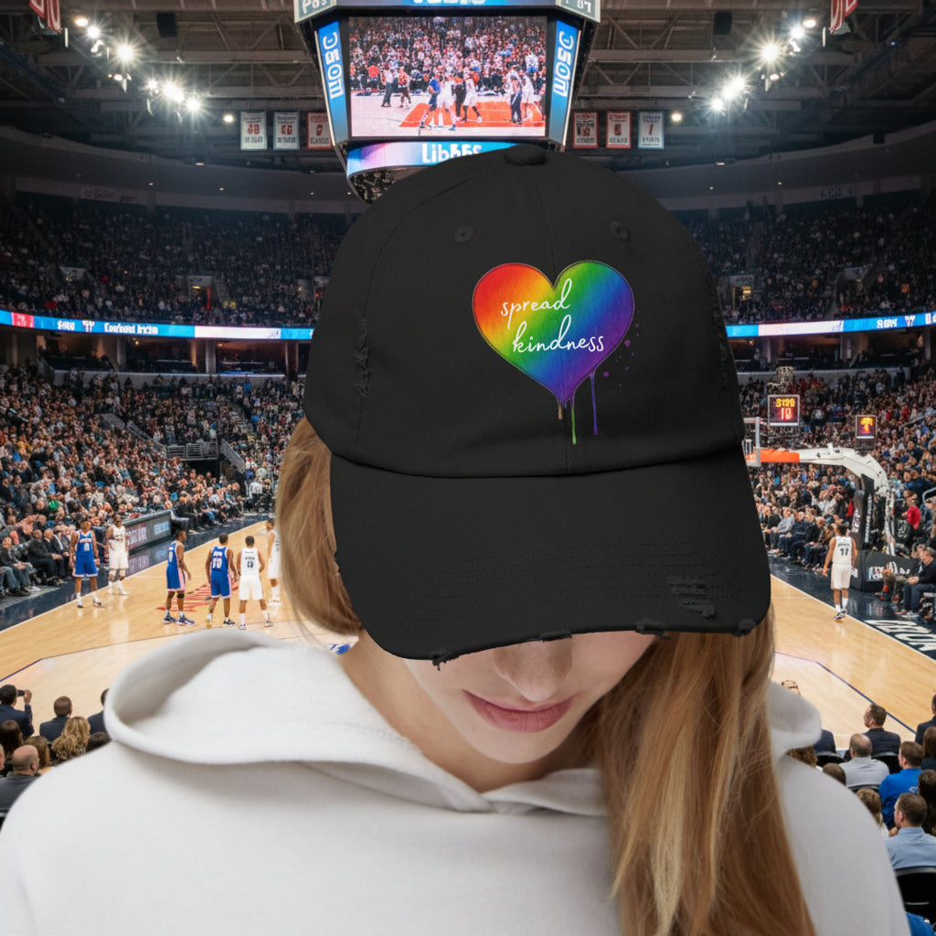 Black cap with a rainbow heart and 'spread kindness' text at a basketball stadium