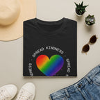 Black t-shirt with rainbow heart and 'Spread Kindness' text on a light surface with casual items.