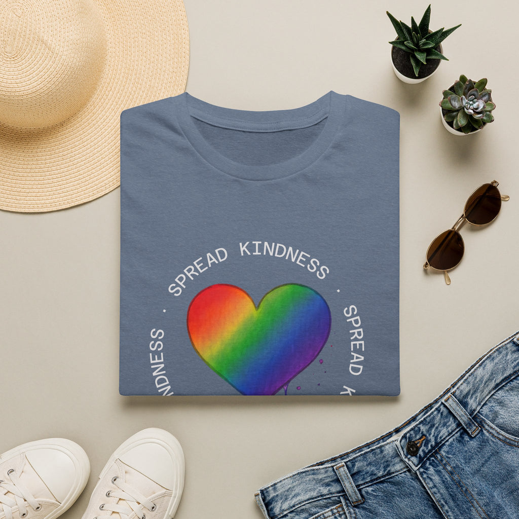 Folded blue t-shirt with rainbow heart and 'Spread Kindness' text on a light surface with accessories.