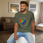 Man wearing a green t-shirt with a rainbow heart design and text in a living room.