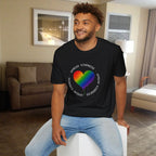 Man wearing a black t-shirt with a rainbow heart design and text in a living room.