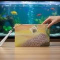 Clutch bag with ocean floor and a sunfish stamp design with a woman's hand grabbing it and an aquarium on the background