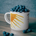 White mug with sun design filled with blueberries on a wooden surface.