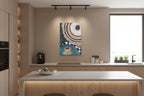 A modern kitchen interior with a colorful abstract wall art print hanging above a light wood countertop. The artwork features concentric circular patterns in blue, beige, brown, black, and white with a coffee cup motif.