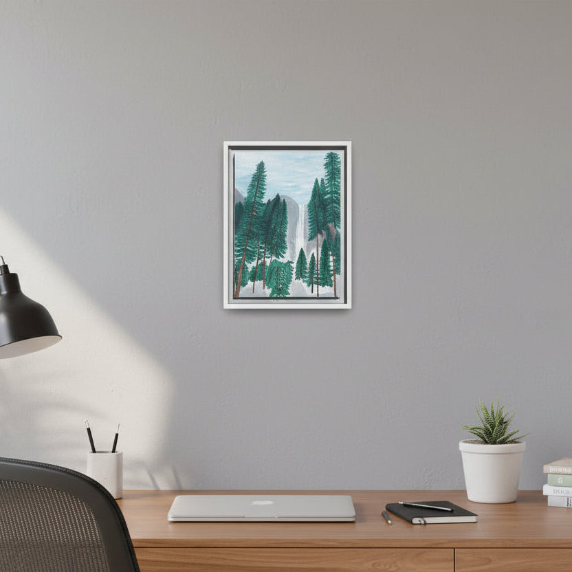 Framed artwork of a forest scene on a wall above a desk with a plant and books.