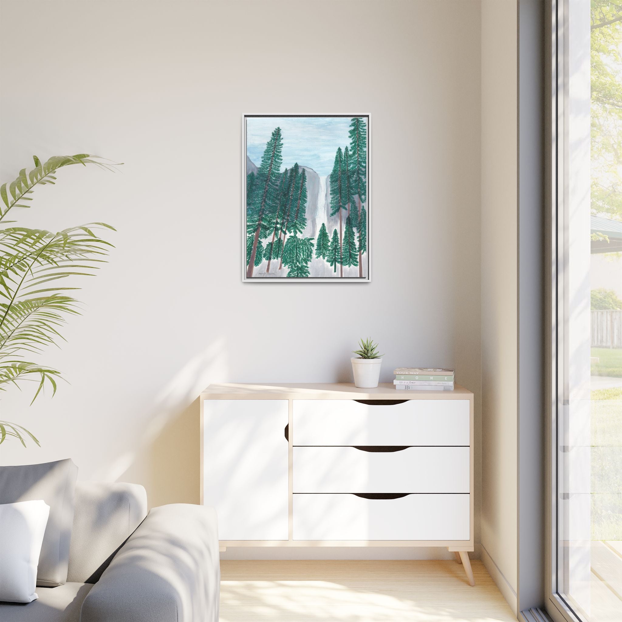 Modern living room with a white dresser, plant, and framed nature print on a light wall.