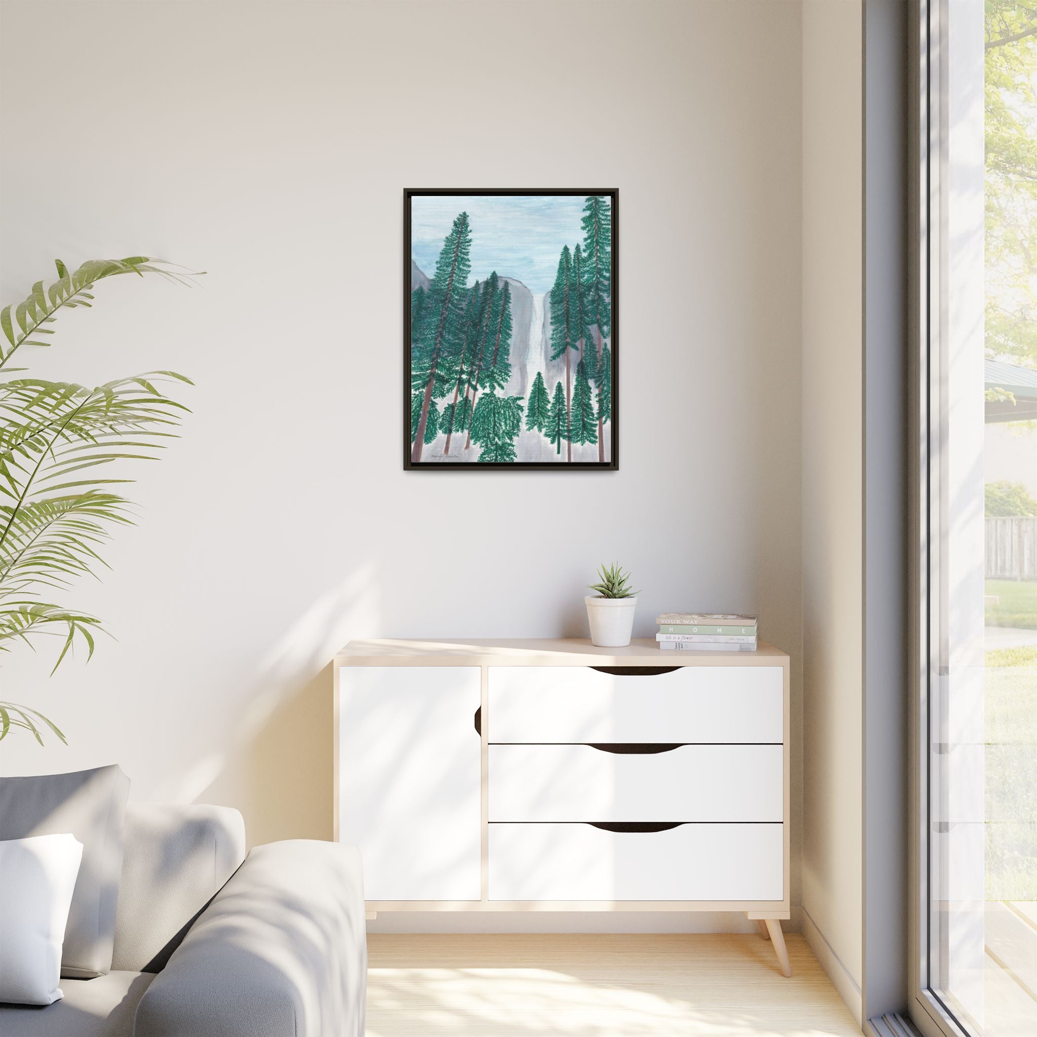 Framed artwork of a forest scene on a wall above a white dresser.