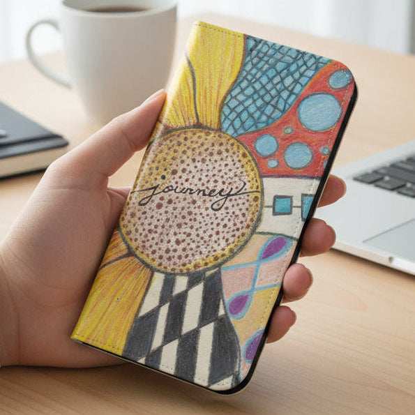 Phone case with Zentangle journey sunflower design held by a person working at a desk with a laptop, coffee cup and notebook and pen.