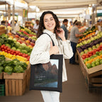 A woman wearing a light beige jacket and white jeans holds a black canvas tote bag featuring a scenic print of Zion National Park.