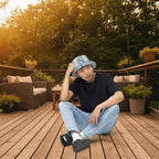 Person wearing a colorful bucket hat, black t-shirt, blue jeans, and black shoes on a white background
