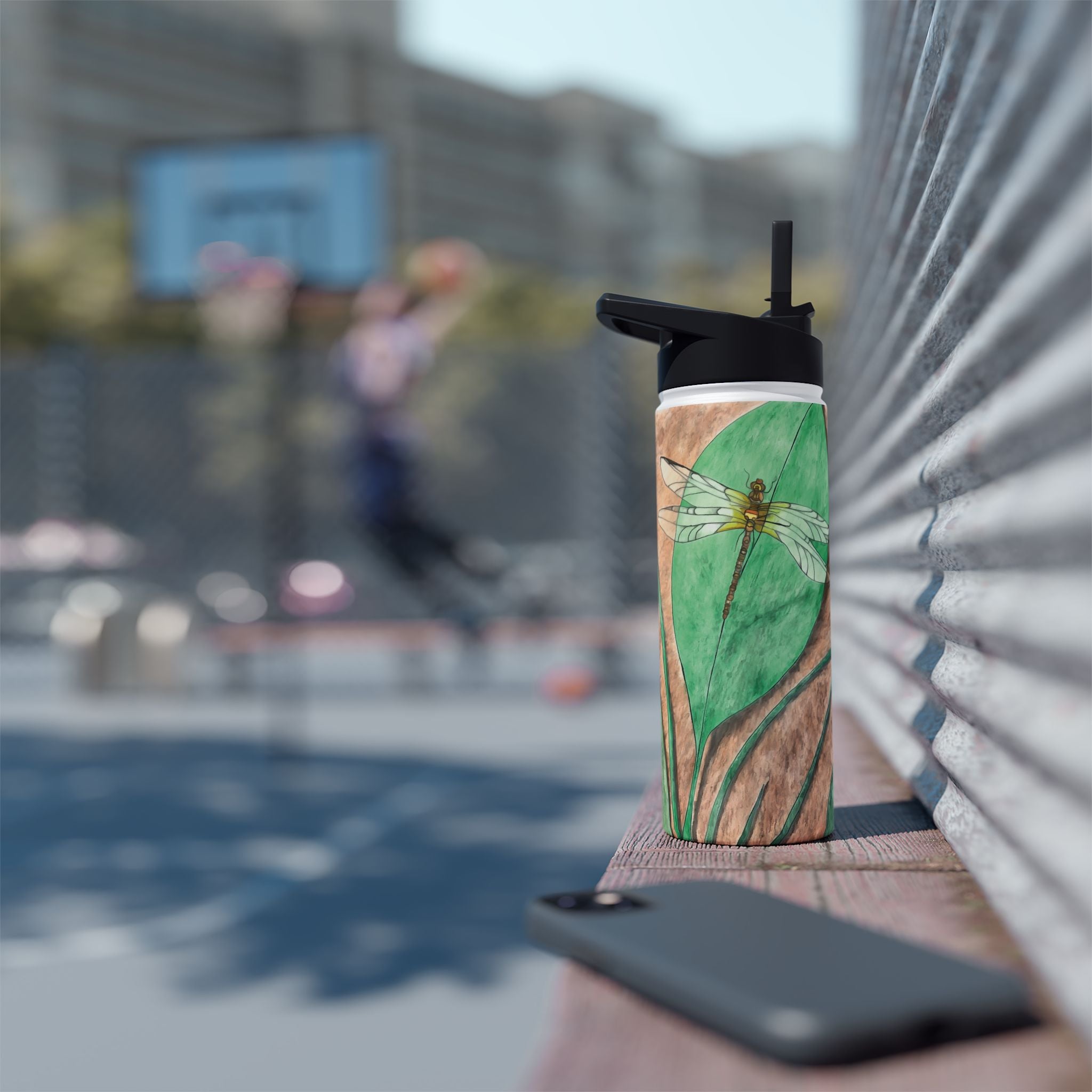 Tumbler with dragonfly design held by a person, blurred background of a basketball game