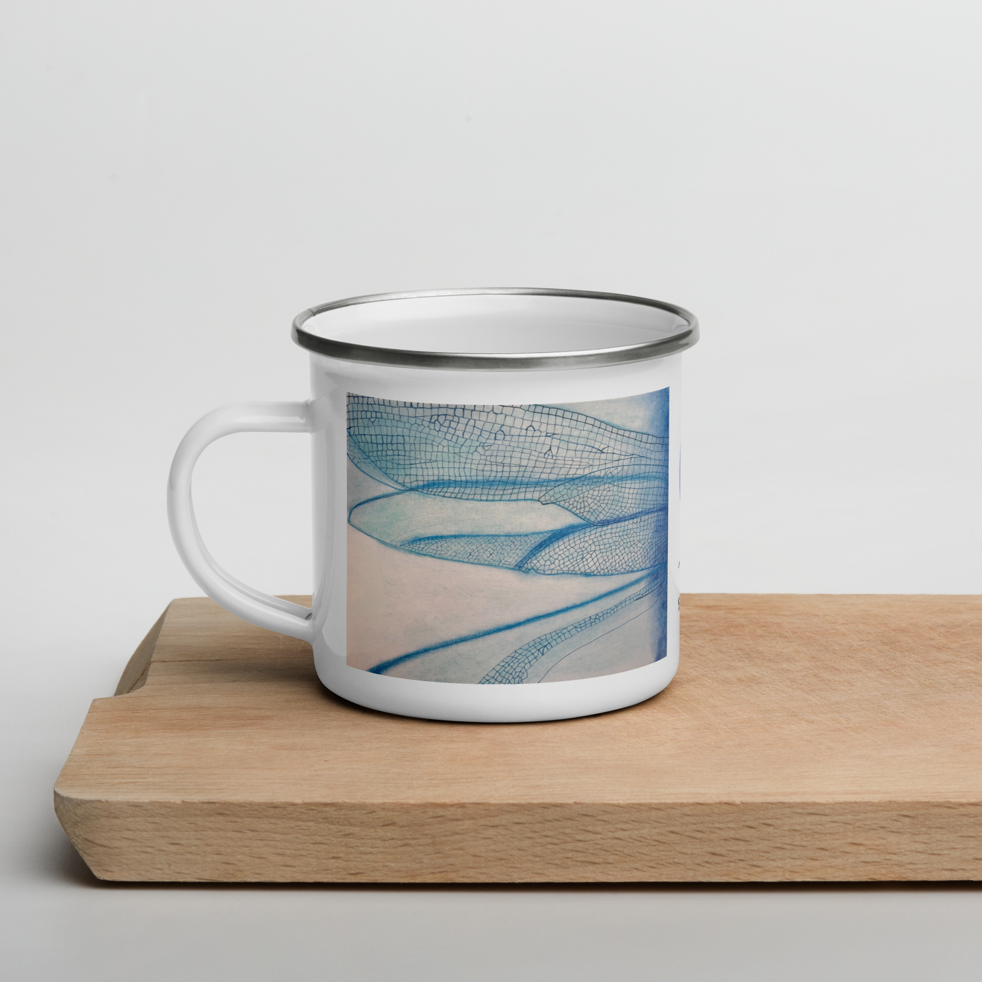 Enamel mug with blue dragonfly wings design on a wooden surface