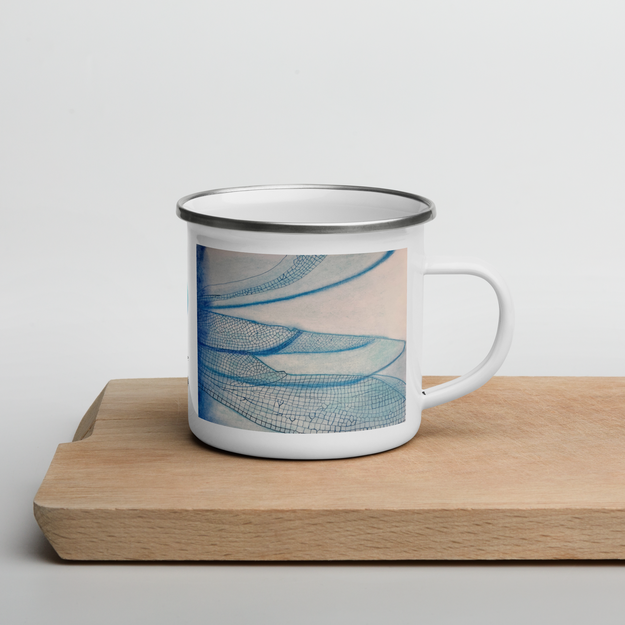White enamel mug with blue dragonfly wings design on a wooden surface