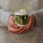 Hands holding a candle with a nature-themed design on a soft fabric background