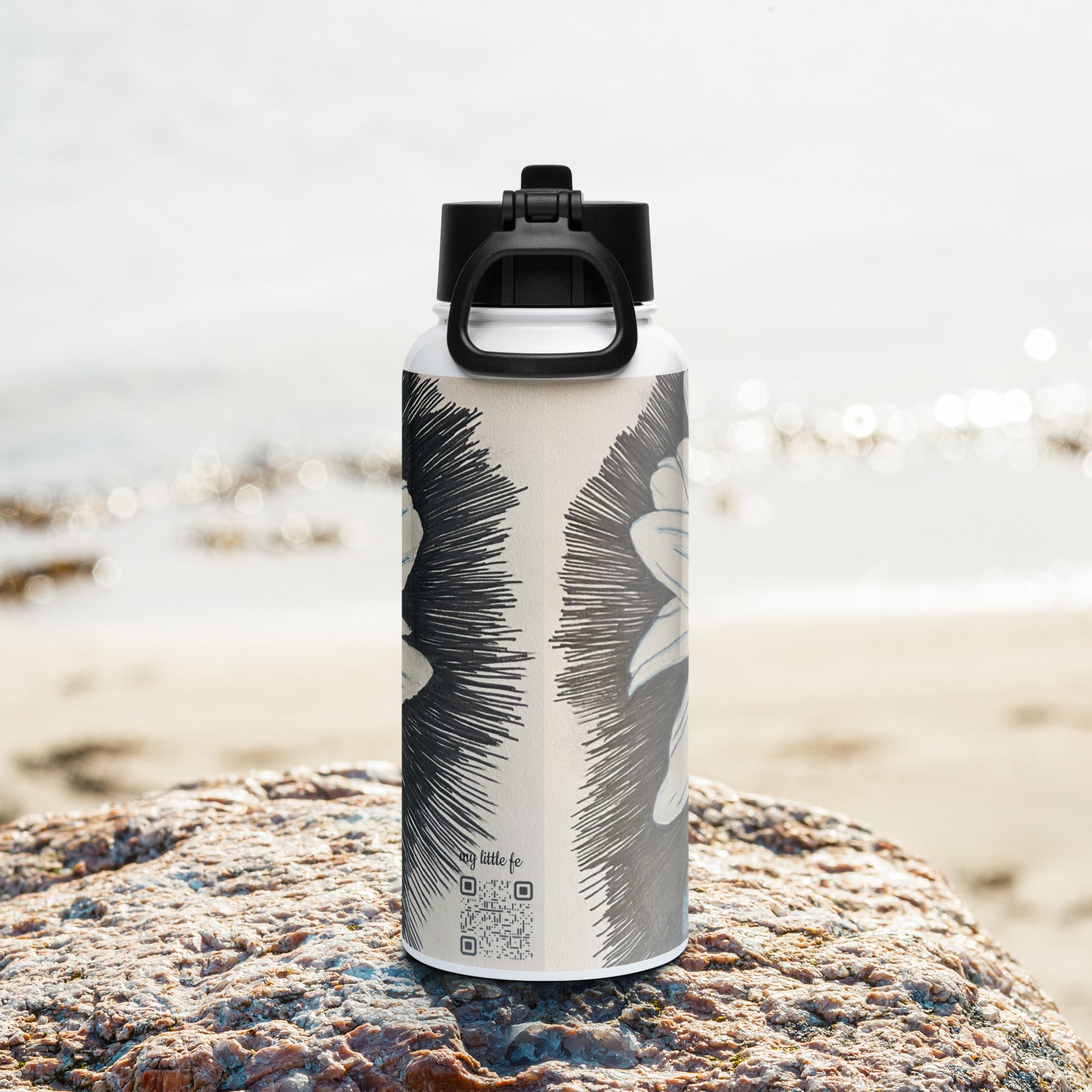 Back side of Water bottle with floral and dragonfly wings design on a rock by a beach