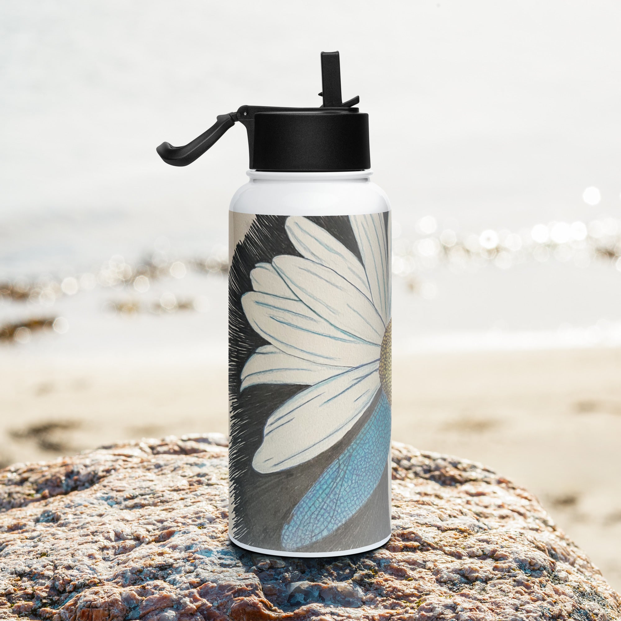 Water bottle with floral design on a rock by a beach
